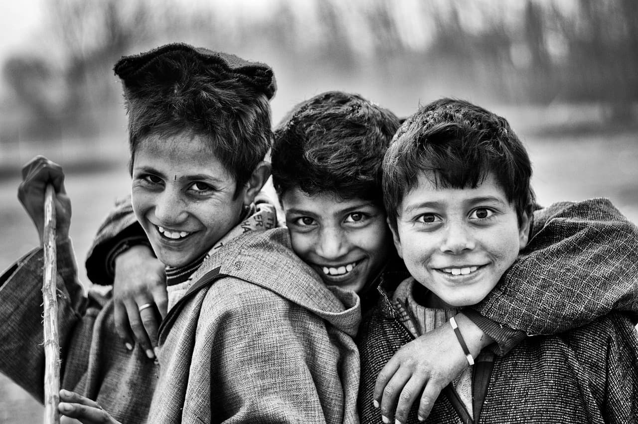 Tres niños riendo y abrazándose, con camisetas coloridas, en la sala de chat de Arab