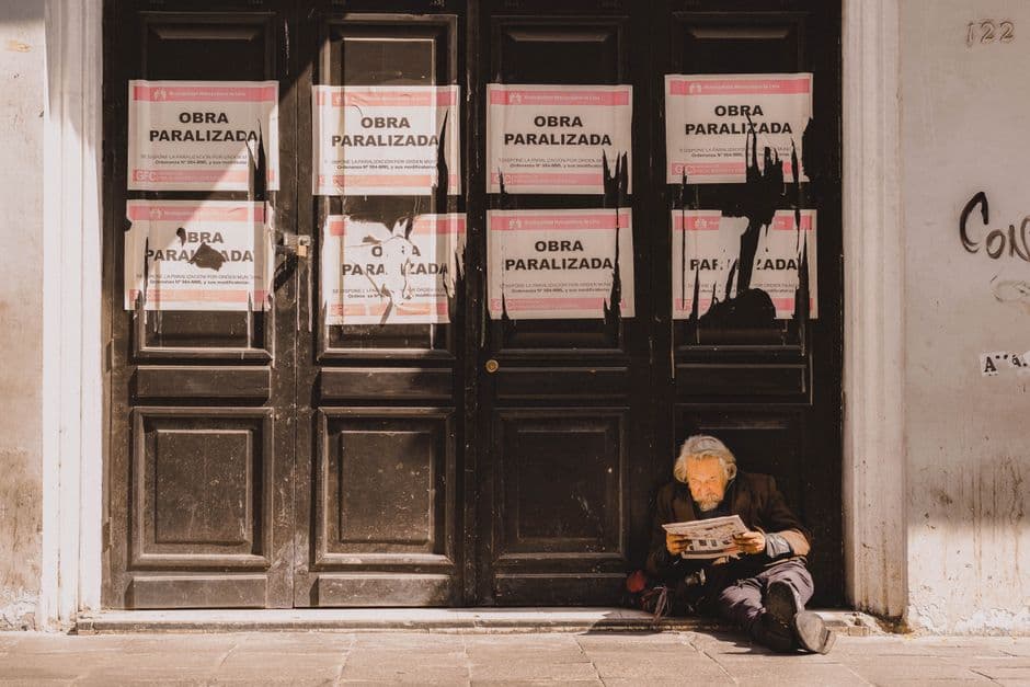 Un hombre mayor sentado en la acera leyendo un periódico