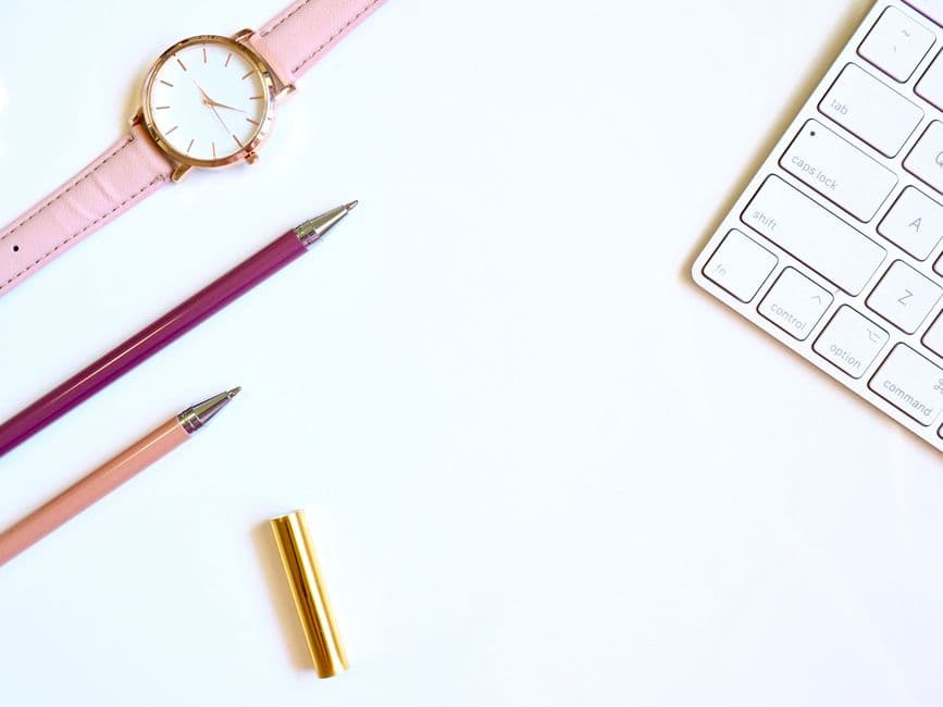 Un reloj redondo de color dorado junto a dos bolígrafos