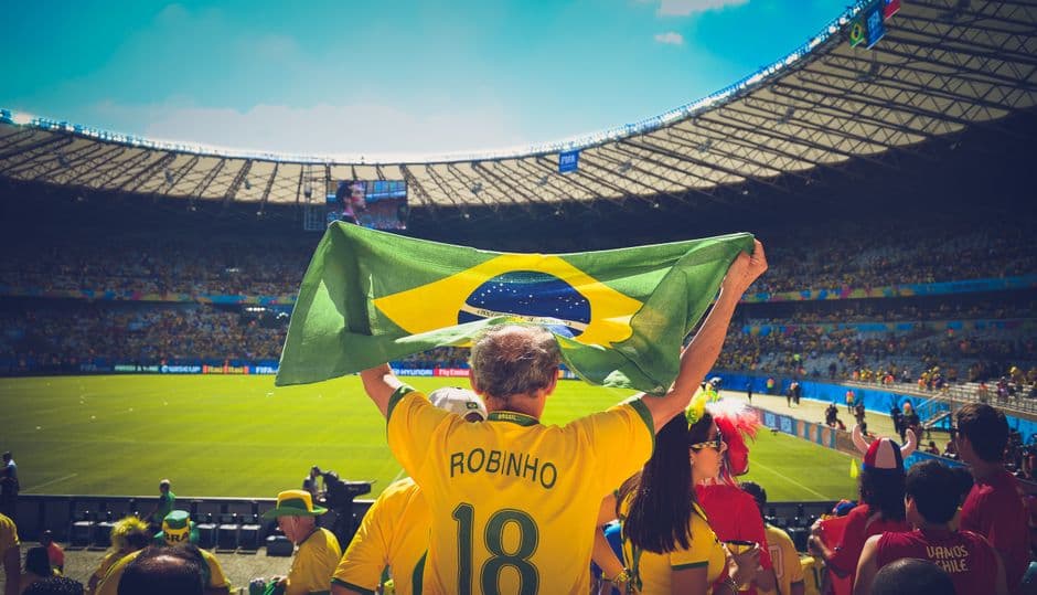 Un hombre levantando una bandera de Brasil dentro de un estadio de fútbol