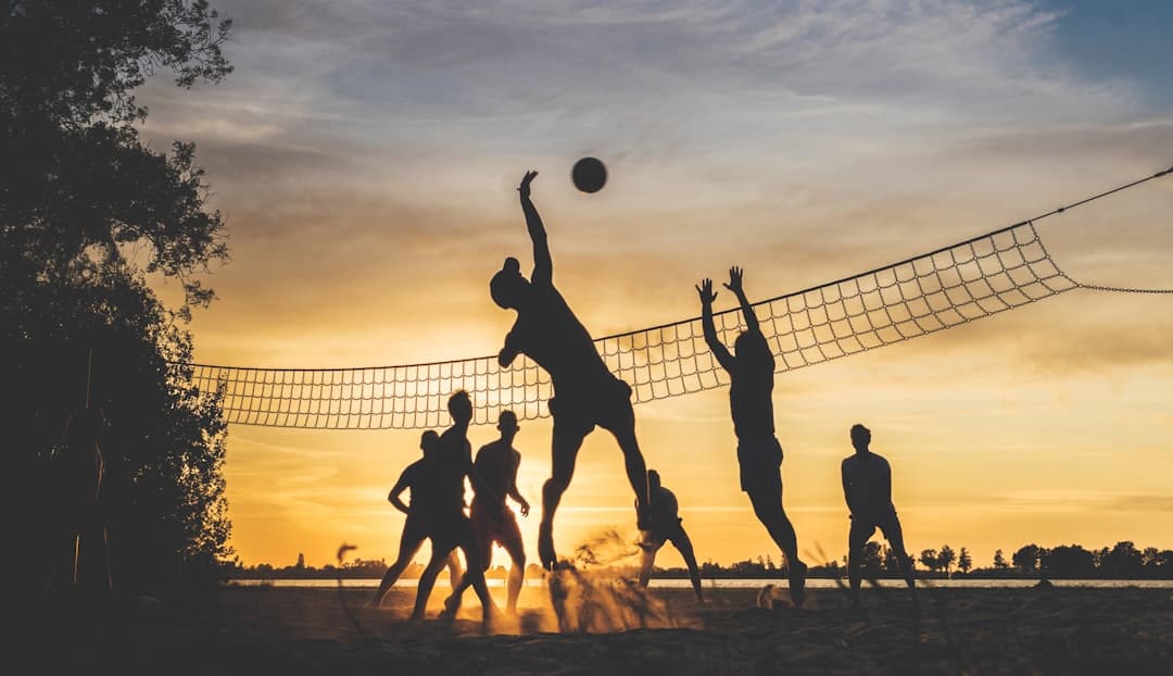 Partida de voleibol en la playa durante el atardecer con cielo naranja