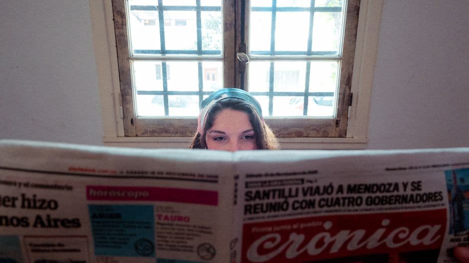 Mujer leyendo un periódico junto a una ventana iluminada por la luz solar