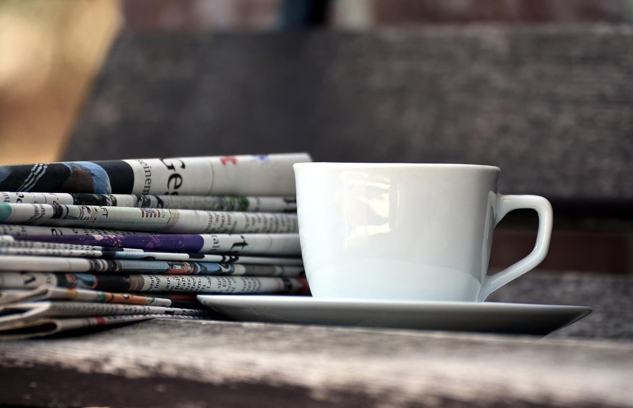 Taza de café rodeada de periódicos y revistas sobre la mesa