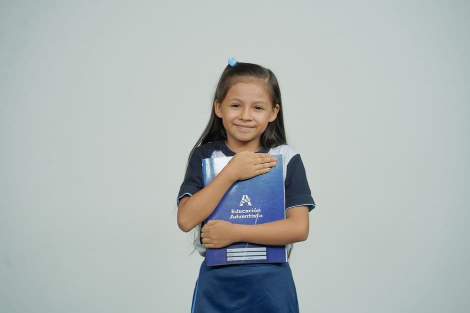 Niña sonriente sosteniendo un libro de texto escolar