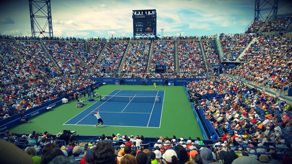 Personas sentadas en banco viendo un evento de tenis durante el día