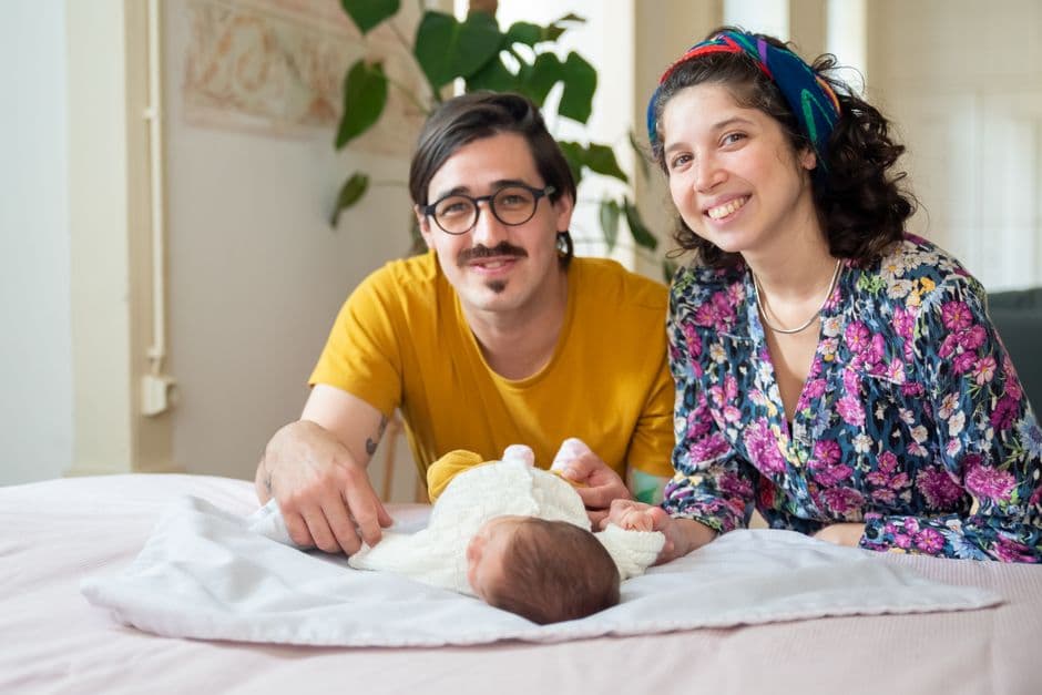 two parents looking at the camera together with their baby