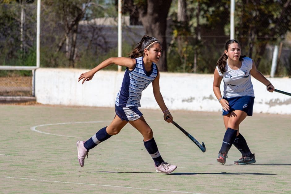 Niñas jugando hockey sobre hierba en cancha deportiva al aire libre