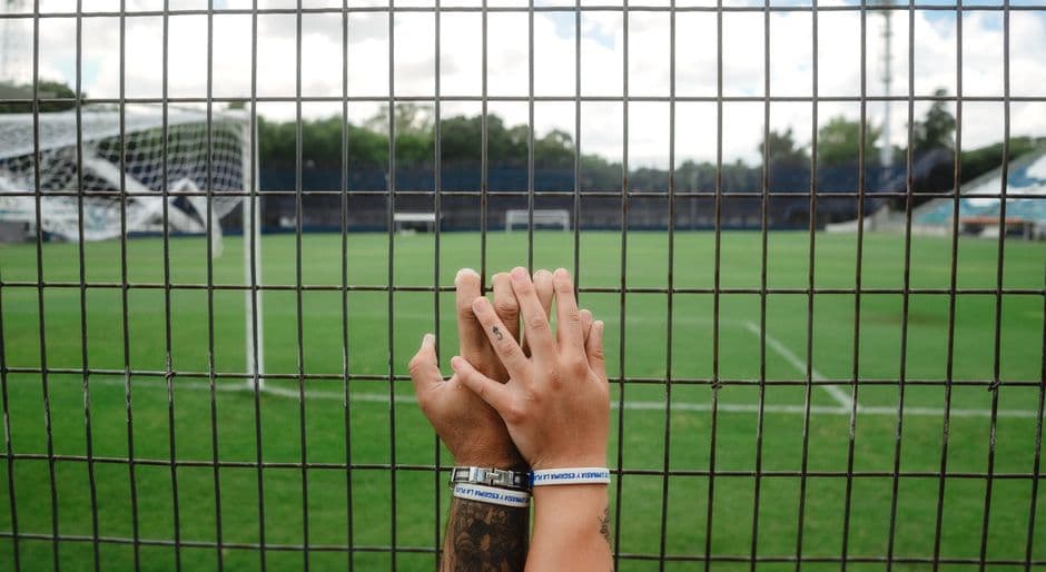 Manos sujetando la valla de un estadio de fútbol