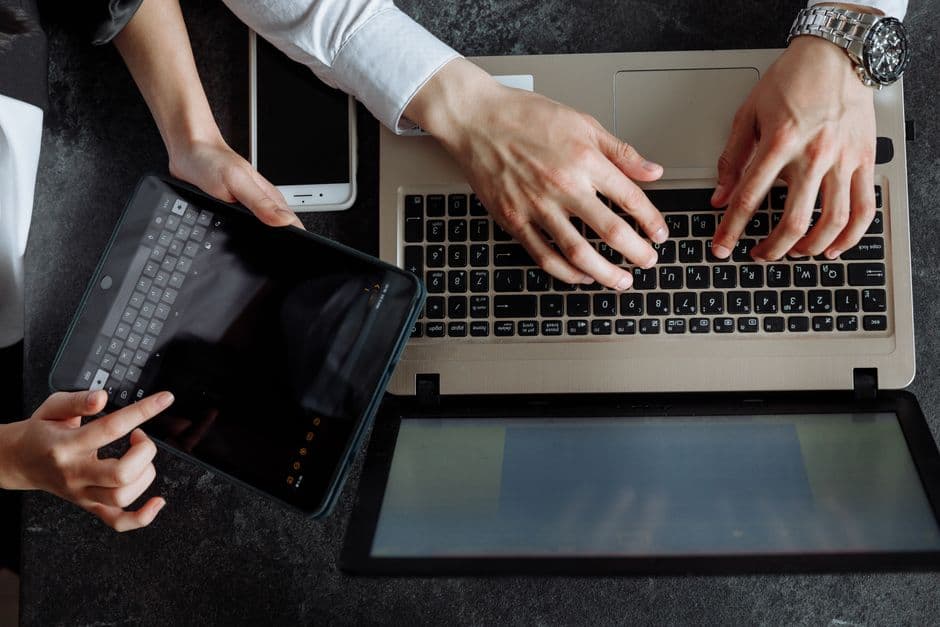 Personas escribiendo en portátil y tableta en escritorio compartido