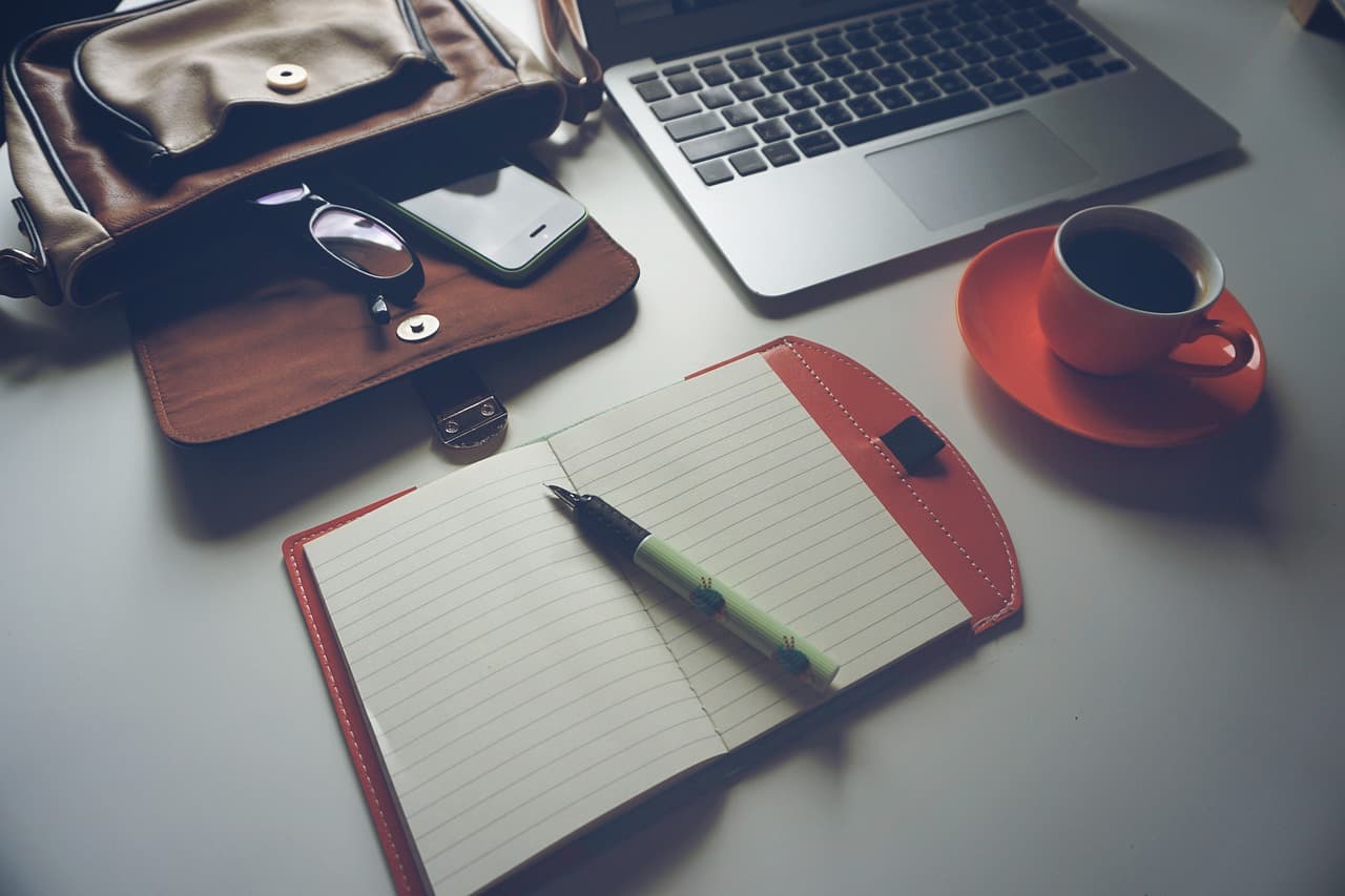 Portátil, café, cuaderno, bolígrafo y gafas sobre mesa