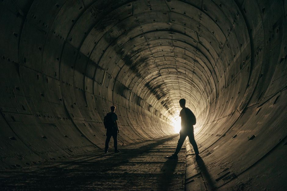 Dos personas caminan dentro de un túnel oscuro con luces tenues