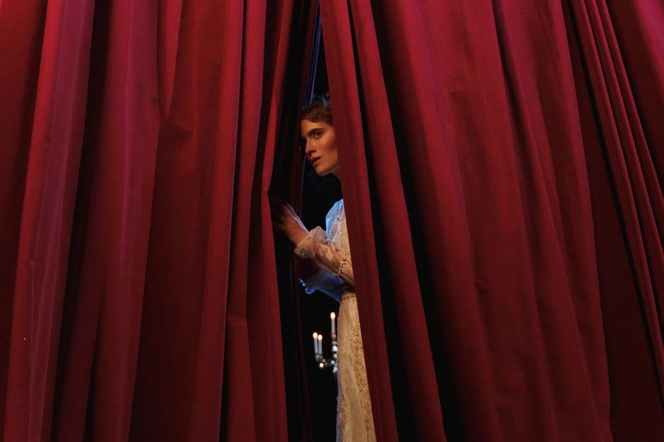 Una mujer de pie tras un telón rojo teatral