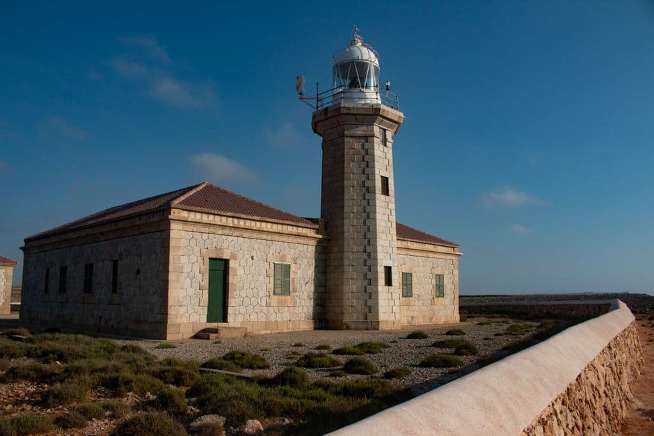 Edificio de hormigón beige junto a un faro, en la sala de chat de Formentera