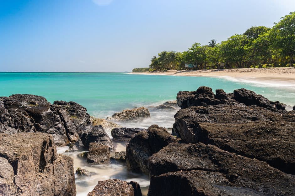 Playa arena, rocas y agua azul bajo cielo claro, en la sala de chat de Honduras
