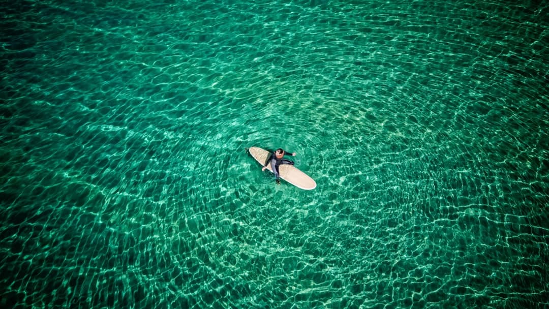 Mujer surfando sobre aguas tranquilas bajo cielo despejado, en el chat de Sanxenxo