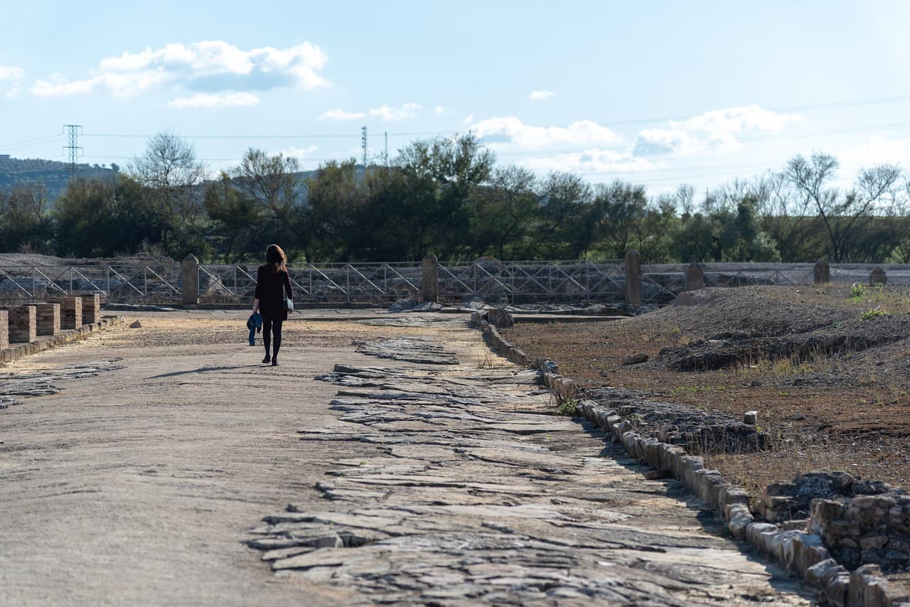 Mujer caminando por una carretera romana entre ruinas, en el chat de Cantillana