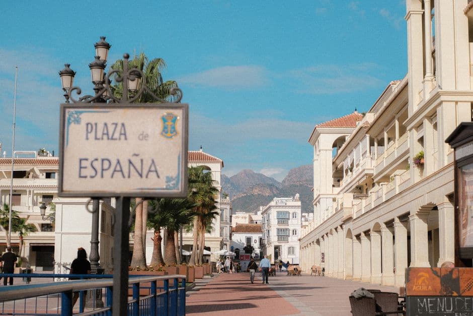 Plaza encantadora con arquitectura tradicional, flores coloridas y gente paseando, en el chat de Benahavís