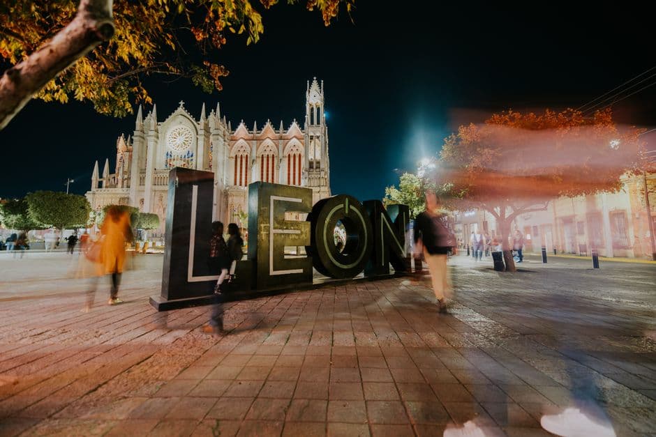 Personas bajo luces entre edificios iluminados, en la sala de chat de León de Los Aldama
