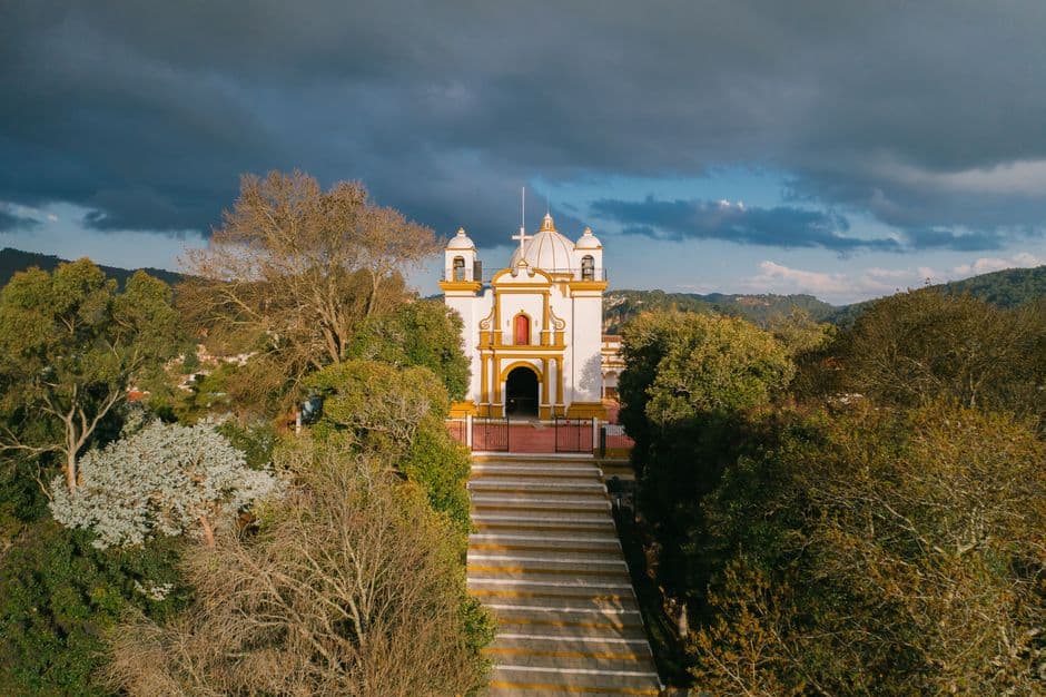 Edificio de hormigón rodeado de árboles bajo cielo azul, en el chat de San Agustín Loxicha
