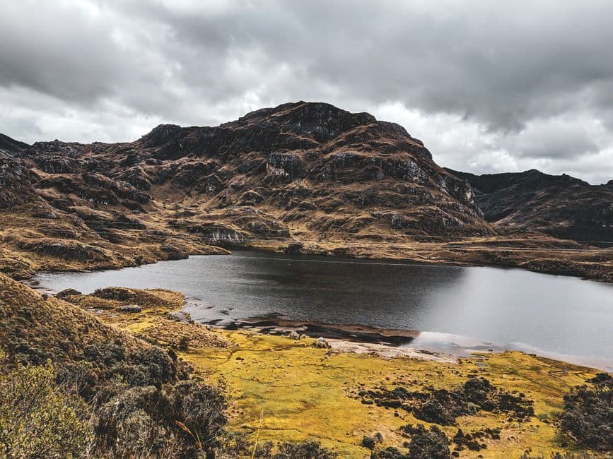 Montaña marrón junto a un cuerpo de agua bajo cielo nublado, en el chat de San Agustín de Cajas