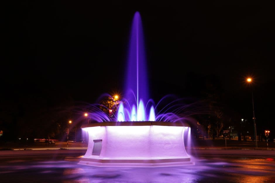 Fuente iluminada con luces entre edificios nocturnos, en la sala de chat de Fuente de Cantos