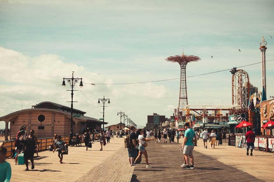 Paseo de Coney Island bajo sol, con gente, ruedas y mar, en el chat de Frisco