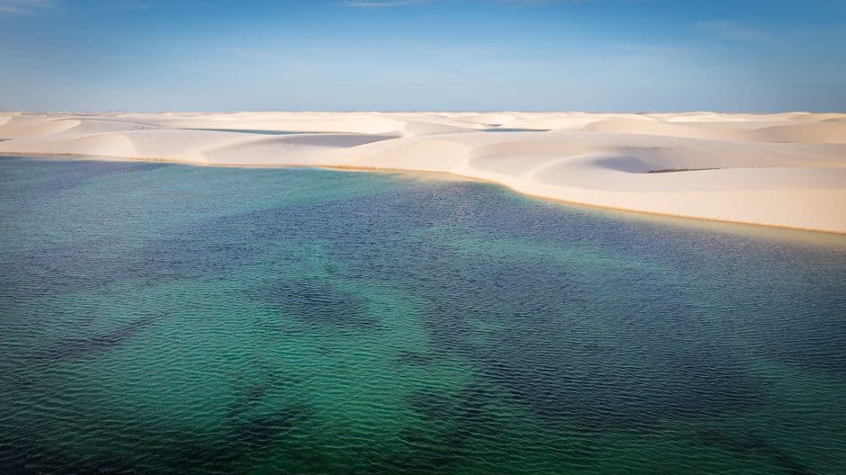 Laguna azul rodeada de dunas de arena bajo cielo claro, en el chat de Sete Lagoas
