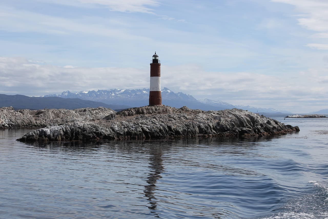 Faro sobre rocas bajo cielo gris, con olas rompiendo, en el chat de Caucete