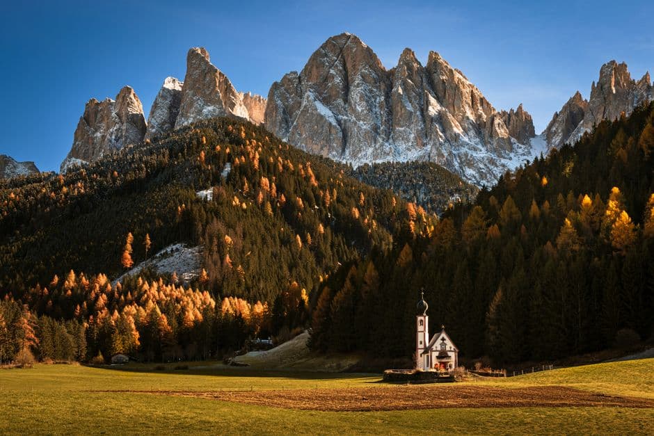 Iglesia de montaña rodeada de árboles otoñales bajo nieve, en el chat de Funes
