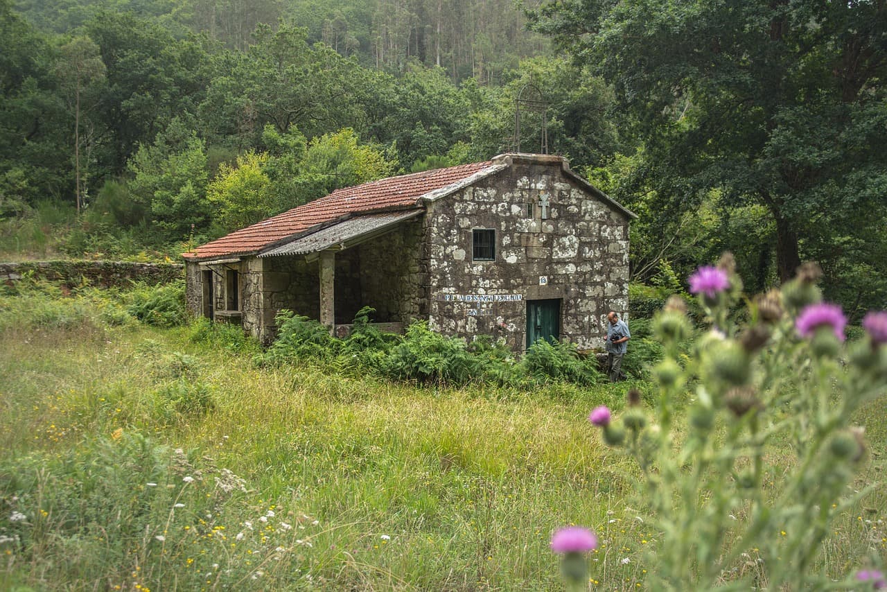 Capilla de piedra con techo de tejas y cruz, en el chat de Mazaricos