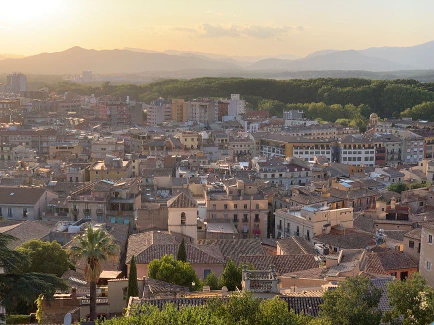 Atardecer sobre el paisaje urbano con montañas al fondo, en el chat de Sant Julià de Ramis