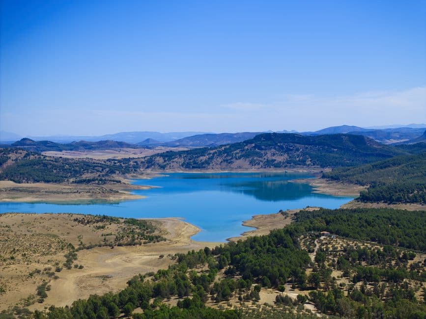 Lago rodeado de colinas verdes bajo cielo azul, en el chat de Teba