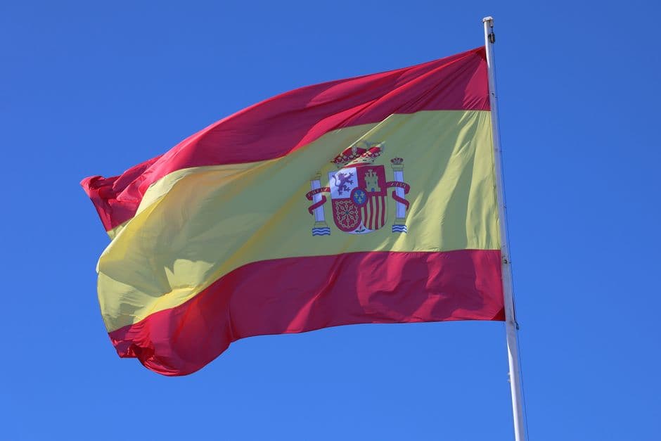 Bandera española ondea bajo cielo azul claro, en la sala de chat de As Neves