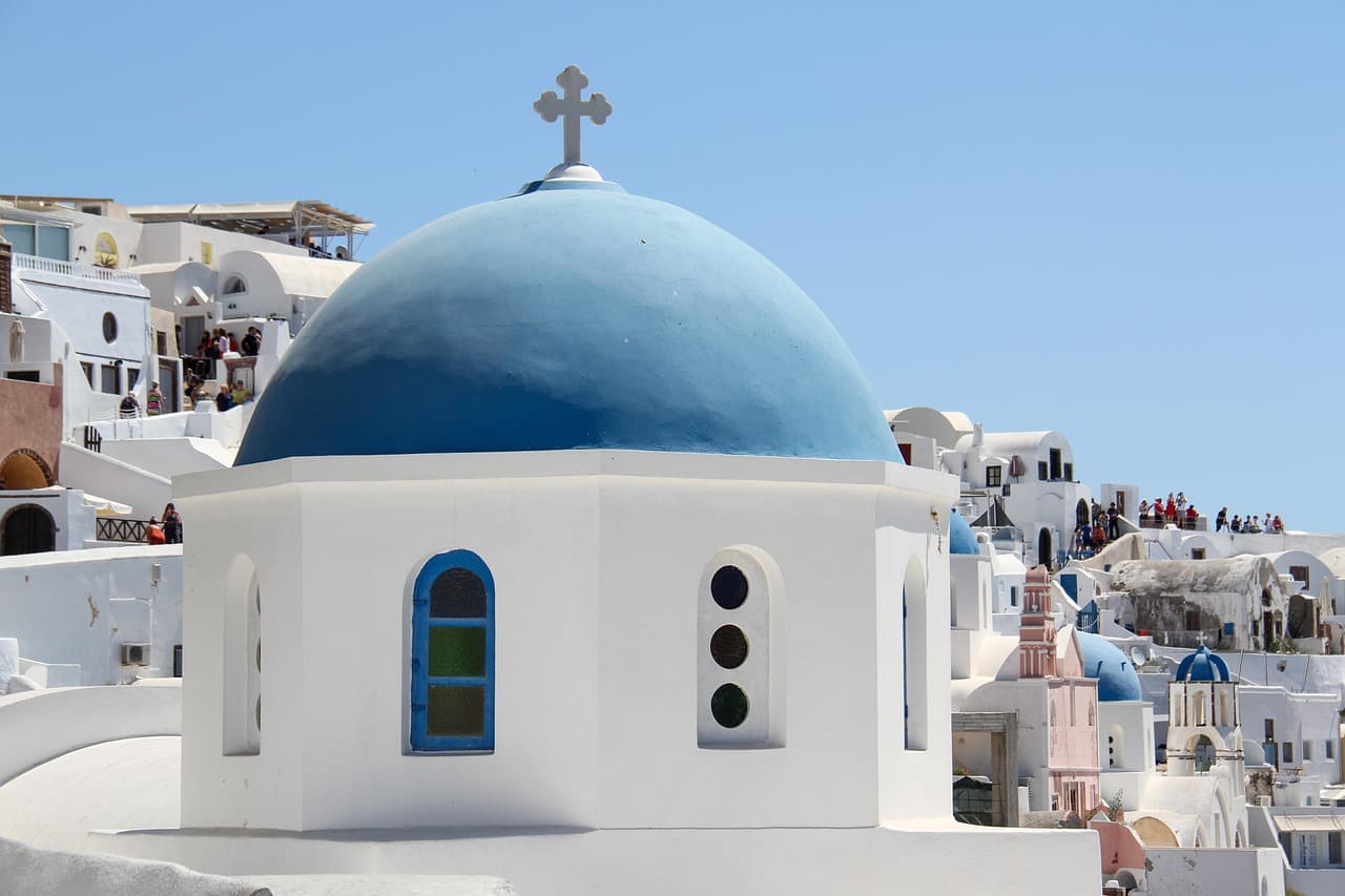 Iglesia blanca con cúpula azul en calle empedrada de Oia, en el chat de Oia