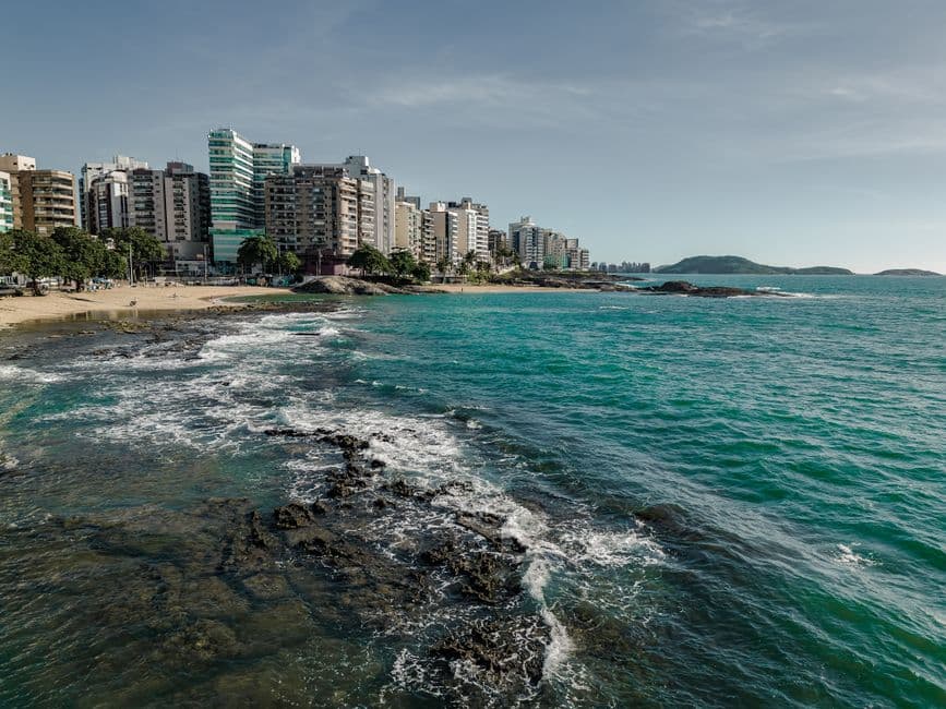 Playa urbana con arena, olas y edificios de fondo, en el chat de Guarapari