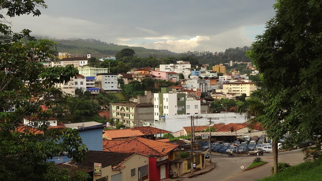 Vista panorámica de edificios y colinas bajo cielo azul, en el chat de Itabira