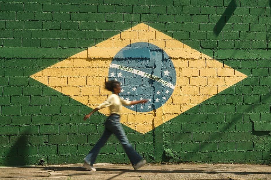Joven camina por la calle junto a pared con bandera brasileña, en el chat de Passos