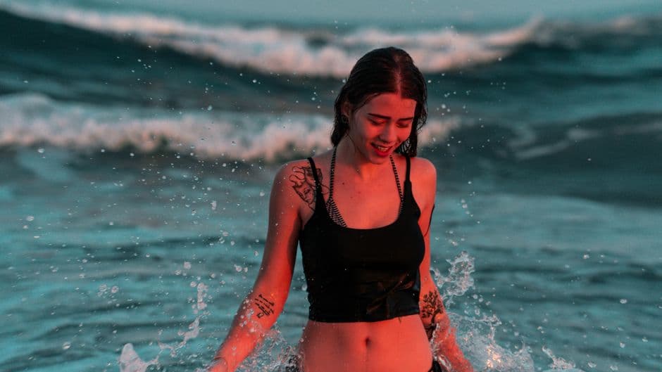 Mujer con camiseta negra de tirantes dentro del mar, en el chat de Cubatão