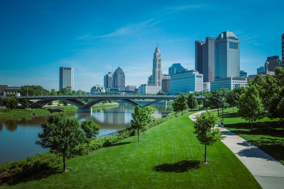 Parque con árboles y senderos junto al río y edificios modernos, en el chat de Columbus