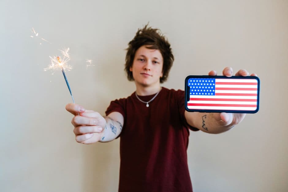 Joven sostiene bengalas y un smartphone con bandera de EE. UU., en el chat de Brandon