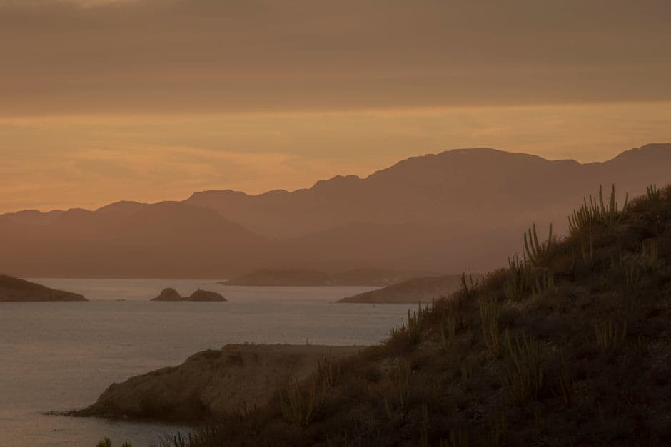 Colinas onduladas junto al mar bajo un cielo rojo al atardecer, en el chat de Sonora