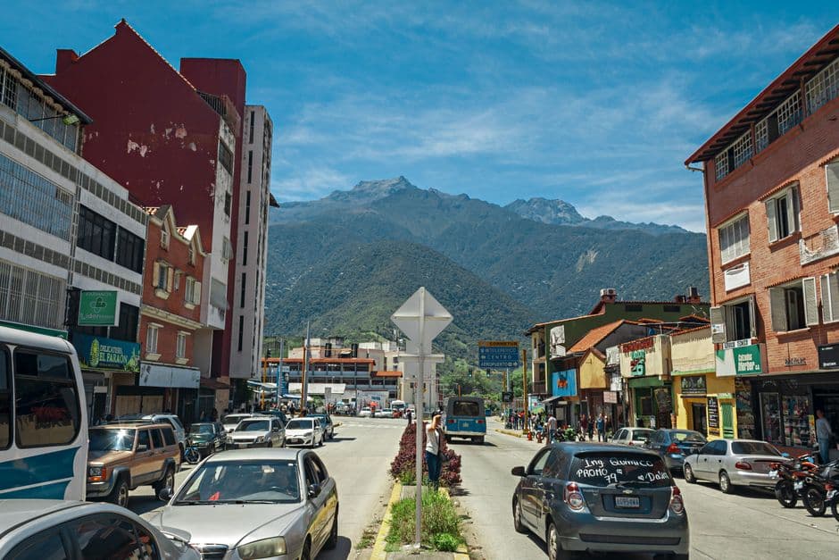 Calle con coches aparcados y edificios de la ciudad, con montañas al fondo, en el chat de Charallave