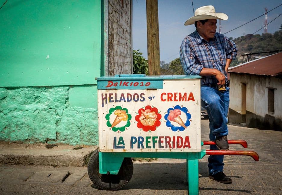 Hombre con camisa de cuadros junto a su carrito de helados, en el chat de San Juan Sacatepéquez