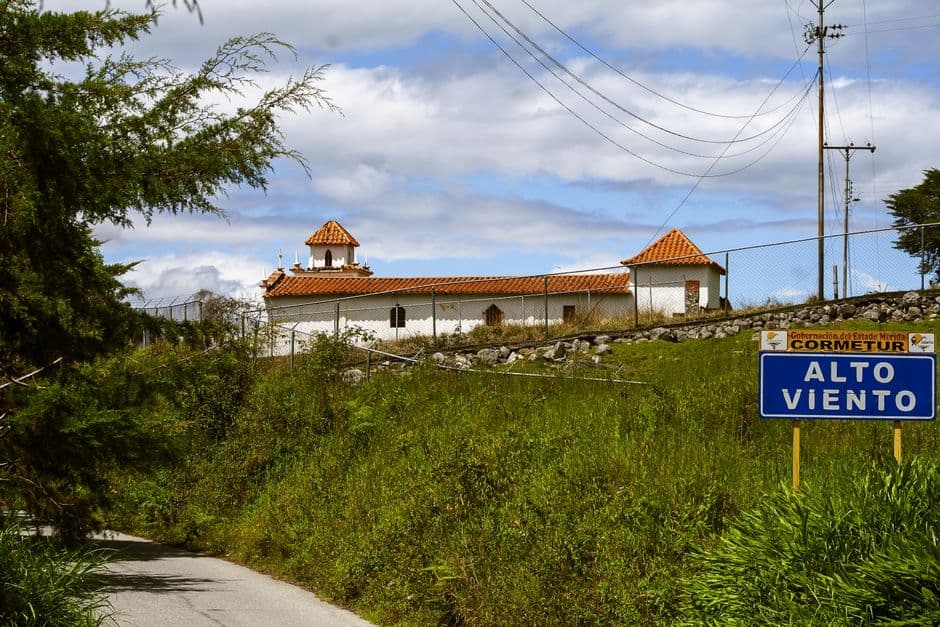 Casa de hormigón blanca y marrón entre árboles verdes bajo un cielo azul, en el chat de Tucupita