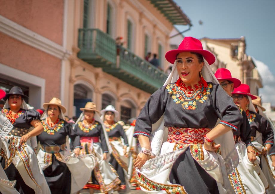Mujeres con trajes coloridos y sombreros rojos en un desfile, en el chat de Samborondón
