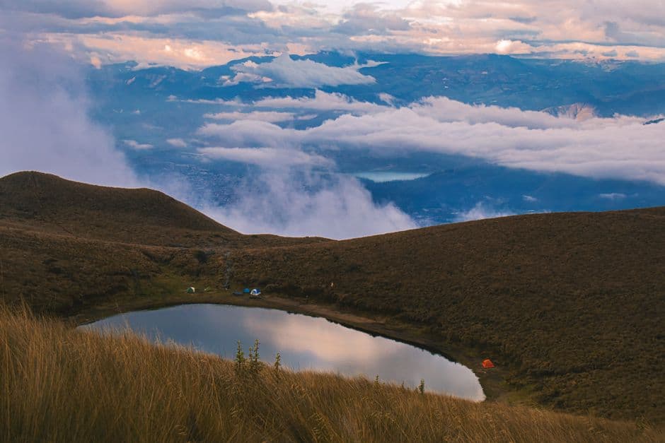 Excursionistas acampan a orillas de un pequeño lago de montaña sobre un valle con niebla, en el chat de Montecristi