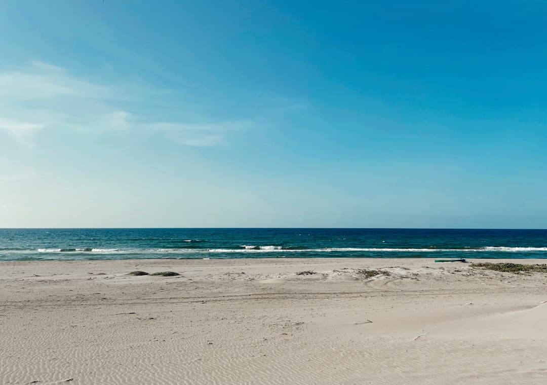 Playa de arena junto al océano bajo un cielo azul, en el chat de Tela