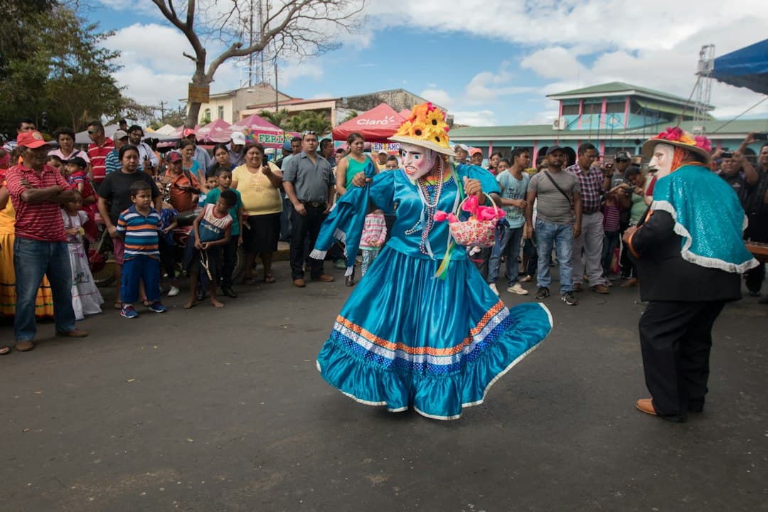 Niña con vestido rojo y azul de pie sobre suelo de cemento gris, en el chat de Diriamba
