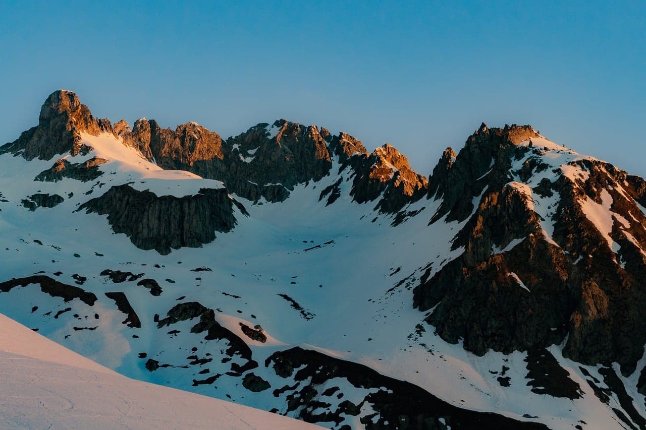 Montaña nevada con senderista en la cumbre sobre un valle amplio, en el chat de Conguaco