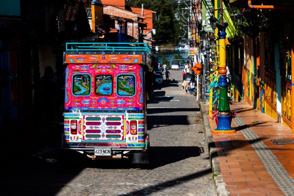 Autobús multicolor circula por una calle urbana con edificios, en la sala de chat de Chía